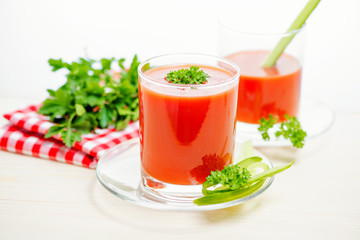 tomato juice in transparent glasses with parsley, cucumber and napkin on light wooden background, close up
