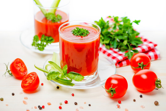 tomato juice in transparent glasses with parsley, basil,  cucumber and napkin on light wooden background, concept vegetarian food, close up
