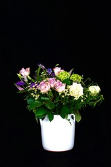 Bouquet of flowers in a white vase against a black background.