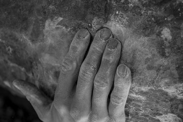 Close up black and white shot of male hand in chalk holding rock wall