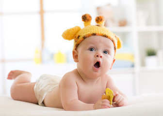 Funny baby boy in giraffe hat lying on his belly in nursery. Little kid lies on bed with opened...