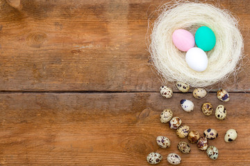 nest with colored Easter eggs and little quail eggs at the old brown unpainted wooden background.