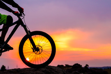 Professional Cyclist Resting with Down Hill Bike on the Rock at Sunset.