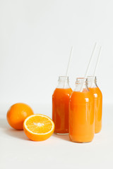 Three bottles of orange juice and tubes are on the table on a white background, as much as two oranges and one orange cut into wooden Boards. Daylight, horizontal image.