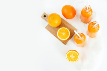Three bottles of orange juice and tubes are on the table on a white background, as much as two oranges and one orange cut into wooden Boards. Daylight, horizontal image.