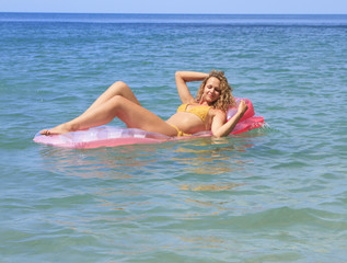 Beautiful young girl floating on a mattress in the sea