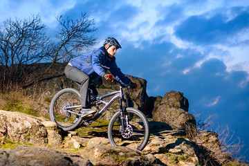 Fototapeta premium Cyclist Riding the Bike on the Rocky Trail at Sunset. Extreme Sport Concept. Space for Text.
