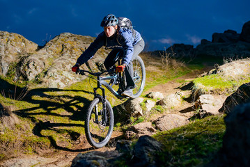 Fototapeta premium Enduro Cyclist Riding the Bike on the Rocky Trail at Night. Extreme Sport Concept. Space for Text.
