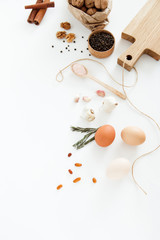 Vegetables, nuts, beans, cinnamon, rosemary, chicken eggs, other food and kitchen appliances lie on a white background. Space for text, daylight, vertical image.