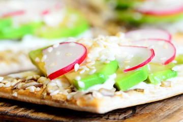 Cracker with sauce and vegetables. Sliced avocado and radishes on crispy cracker with seeds on wooden board. Simple and quick veggie sandwiches. Closeup