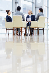 Group of business people sitting in circle during discussion  meeting in glass hall of modern office building