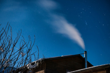 Fototapeta premium White smoke from the house chimney at the winter night sky background