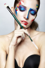 Young female painter with  paint brush in hand  and  acrylic paint on face