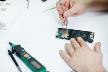 Closeup shot of male hands working on disassembling circuit board in modern mobile phone device on table in maintenance shop with assorted tools