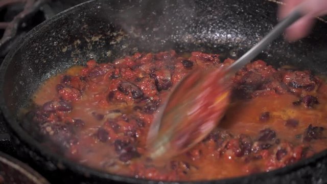 Red kidney beans frying in red sauce in a pan, close-up.