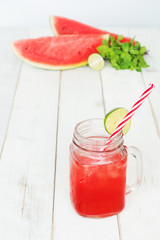 Cold watermelon lemonade / watermelon juice in mason jar with red striped straw, watermelon slices, mint and lime on a white table. Selective focus, copy space.