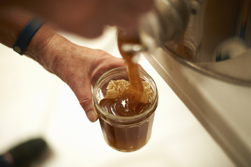 Hands of female beekeeper pouring honey into jar from kitchen vat