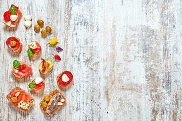 Mix of appetizers / snacks. Mediterranean tapas or antipasti on a rustic wooden table. Sandwiches with salami, jamon, mozzarella, cheese, sardines, salmon, tomato, olives and basil. Copy space.