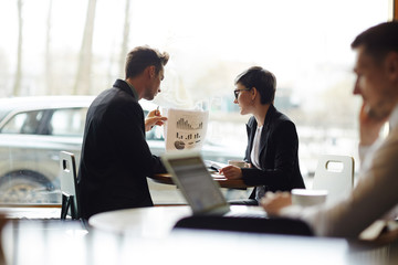 Busy employees in formalwear sitting at cafe window and analyzing statistics, stylish businessman holding document with financial diagrams