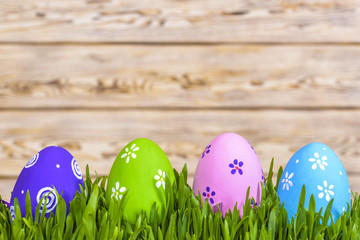 Fototapeta na wymiar Pastel colored easter eggs in green grass over rustic wooden background.