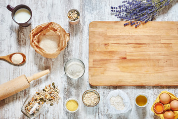 Baking background. Wholegrain flour, eggs, grains and seeds, oat flakes, olive oil, cup of milk, wooden board, spoon, rolling pin on a light rustic table. Copy space.