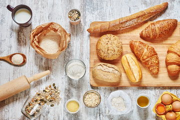 Fototapeta na wymiar Baking background. Set of fresh bread, wholegrain flour, eggs, grains and seeds, oat flakes, olive oil, milk, wooden board, spoon, rolling pin on a light rustic table.