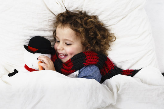 Overhead view of girl lying in bed hugging snowman