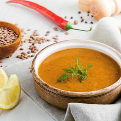 Healthy vegetarian lentil soup in a rustic clay bowl , piece of bread and lemon slices on a white wooden table. Delicious healthy meal served on a canvas tablecloth.