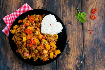 Picadillo, a stew of ground beef and tomatoes, with raisins and olives with boiled rice on a black...