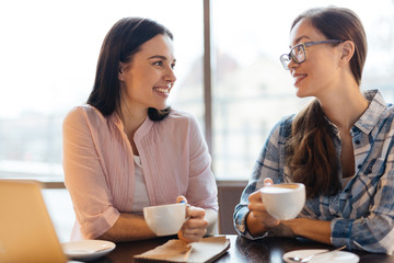 Friendly girls with cups of coffee talking at break