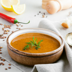 Bowl of delicious lentil soup with bread, lemon slice and spoon on a white wooden table. Traditional healthy vegetarian food.