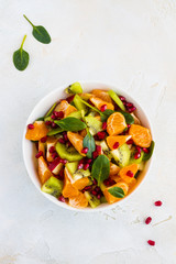 Vitamin fruit salad with fresh apples, tangerines, kiwi, spinach and pomegranate seeds. White bowl on a light concrete table, top view.