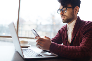 Young banker reading sms while working in cafe