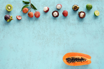 Variety of tropical fruits over blue background. Fresh papaya, kiwi, lime, mangosteen, lychee. Copy space.