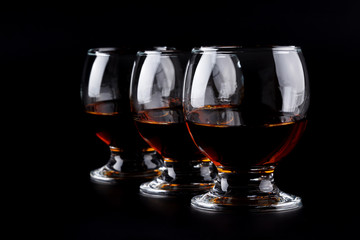 Three glasses with cognac in a row on a black background