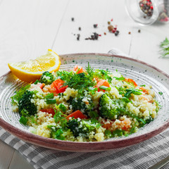 Vegetarian salad made of couscous, broccoli, tomato, pepper, onion and dill on a plate. Traditional Moroccan food for healthy meal on a table.
