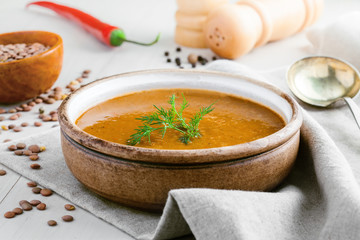 Lentil soup in a rustic bowl on a cotton canvas tablecloth. Healthy vegetarian food on a white wooden table.