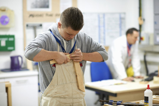 Male teenage carpentry student pushing wood joints together in college workshop