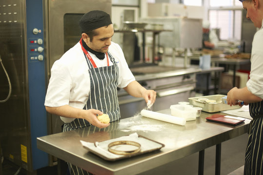 Chef lecturer demonstrating technique to teenage catering student at kitchen counter