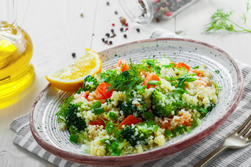 Traditional eastern couscous with broccoli, tomato, pepper, onion and dill on a plate for healthy meal. Moroccan healthy food on a table. Close-up shot.