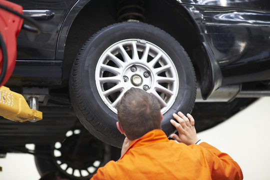 Rear view of college mechanic student inspecting car wheel in repair garage