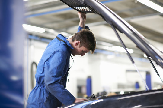 College mechanic student inspecting under car hood in repair garage
