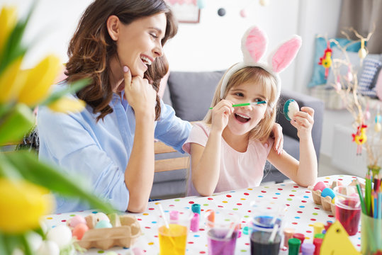 Woman and daughter painting easter eggs at table