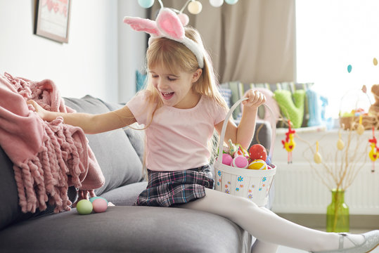 Girl finding easter eggs under sofa blanket