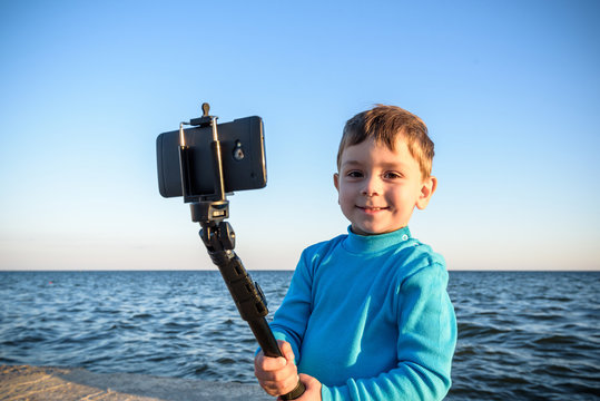 Young boy doing a selfie at the beach, kid happy and smiling looking on mobile phone.