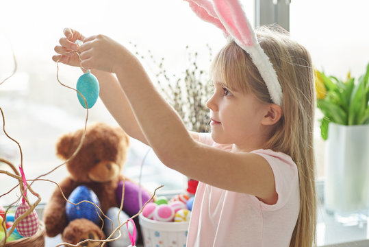 Girl in bunny ears making easter egg decoration in living room