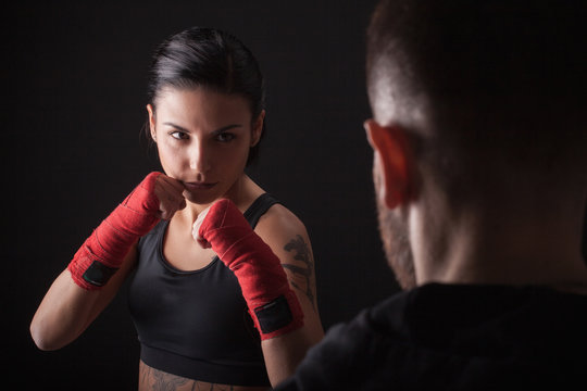 Portrait of young woman in fighting stance, facing fitness trainer