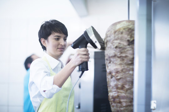 Young woman slicing kebab meat in fast food shop