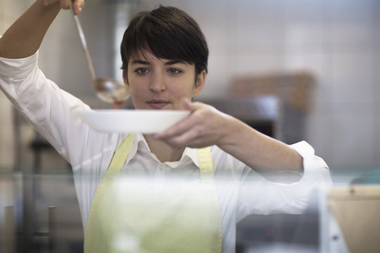 Young woman spooning food into bowl in fast food shop