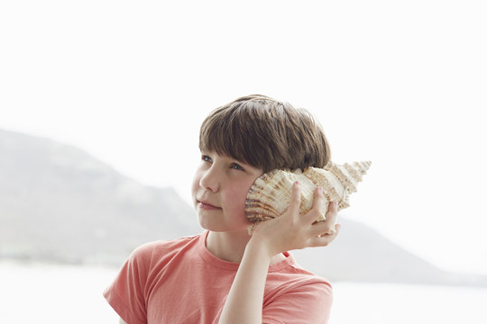Boy holding seashell to ear, Kraalbaai, South Africa